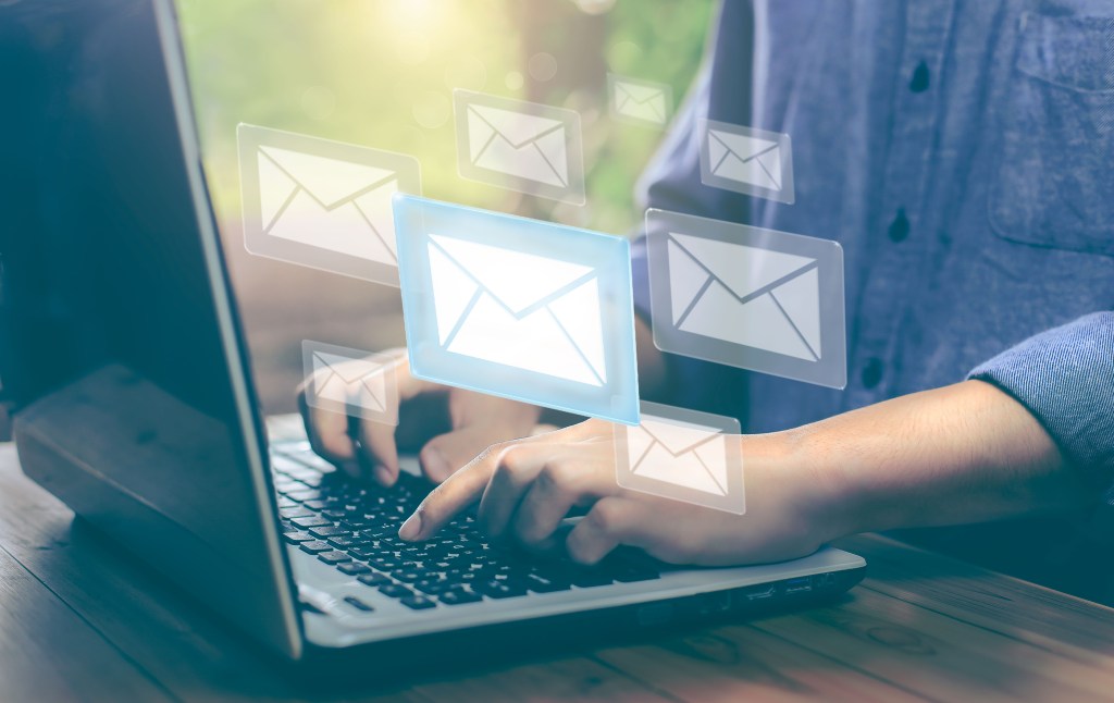 Person typing on a laptop with email illustrations popping up